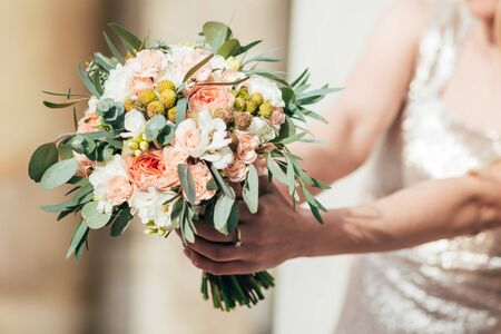 the bride holds the beautiful wedding buoquet with white and peach roses and green eucalyptus leavesの写真素材