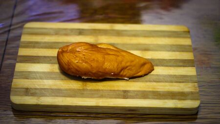 Smoked chicken breast stands on a striped bamboo boardの写真素材