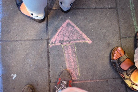 The Arrow Is Drawn In Chalk On The Asphalt, Around It You Can See The Feet Of People In Shoes