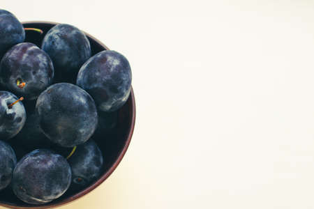 Several ripe blue plums in a deep clay plate on a white background with a copy spaceの写真素材