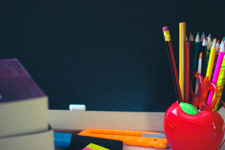 A variety of office accessories on the background of a dark school blackboard. On the board there is...
