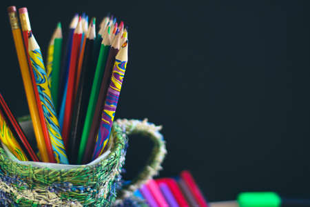 Color pencils and pens on the background of a dark school blackboard. On the board place for a copy space.の写真素材