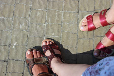 Men's and women's feet shoes in sandals, on a stone pavement in the sunlightの写真素材