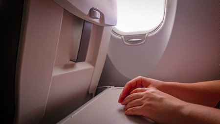 Hands on the folding table of the chair in the cabin of the aircraft near the porthole