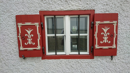 Open vintage red wooden shutters on a small window in a concrete wall