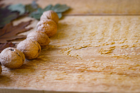 On a wooden background are yellowed oak leaves and walnuts in shell