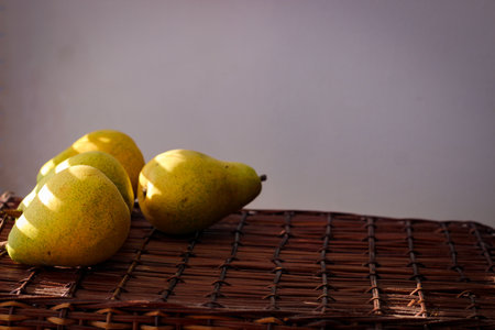 Several ripe yellow pears stand on a wicker basket illuminated by rays of the sunの写真素材