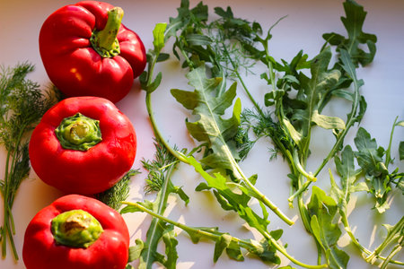 Several juicy red bell peppers and arugula lie in the rays of the sunの写真素材