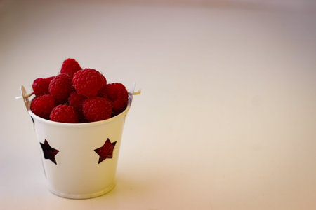 Red ripe and juicy raspberry in a small white bucket with stars