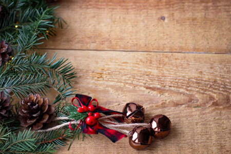 Christmas background. Spruce branches with cones and bells on wooden board