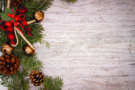 Christmas background. Spruce branches with cones and bells on wooden board