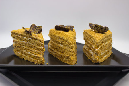 Three layers of honey cake topped with chocolate pieces on a black plate.