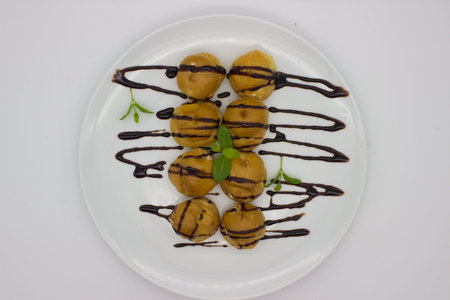 A delectable plate of cream-filled profiteroles, elegantly drizzled with rich chocolate sauce. Garnished with fresh mint leaves, this dessert is both visually appealing and irresistibly delicious.の写真素材