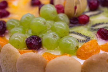 This close-up of a vibrant fruit tart highlights an array of juicy berries, grapes, kiwi, and physalis arranged on a creamy filling. The glaze adds a fresh, glossy texture that enhances the visual appeal of the dessert.の写真素材