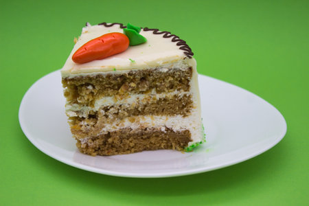 A single slice of carrot cake on a white plate, topped with a marzipan carrot and creamy frosting. Layers of moist carrot cake and filling are visible.の写真素材