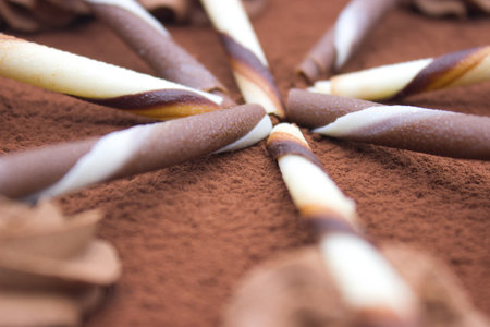 A beautifully layered chocolate mousse cake garnished with chocolate swirls and cocoa powder, served on a white plate. In the background, fresh lilac flowers add a touch of elegance and color contrast.の写真素材