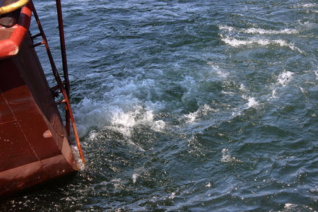 Closeup of ship stern and swirling sea water created by engine movement. Dynamic texture of waves and foam under sunlight.の写真素材