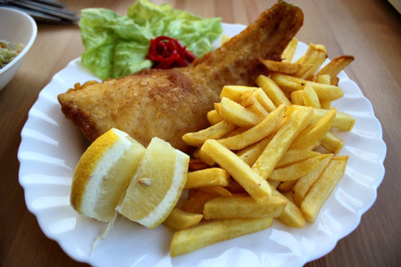 Close-up of a traditional seaside meal with golden fried fish, crispy French fries, and lemon wedges...