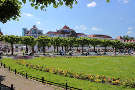 View of the park and public square in front of the Sopot pier with trimmed trees, flowers, and historic buildings under blue summer sky in Poland.の写真素材