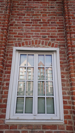Gdansk, Poland. June 07, 2019. Historic red brick facade with white framed window reflecting modern...