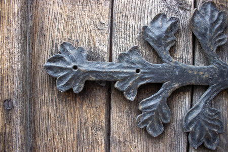Close up of ornate wrought iron hinged mounted on weathered wooden door showing traditional...