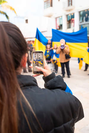 Estepona, Andalusia, Spain -  March. 05, 2022. Protestors rally in support of Ukraine against russian agression. Anti-war demonstration. Woman makes a picture with her phone.のeditorial素材