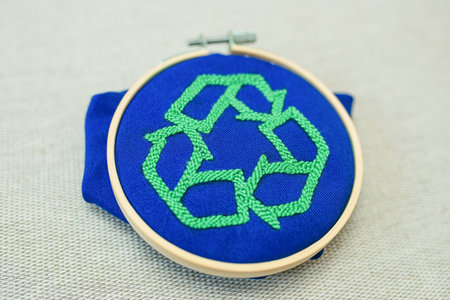 Closeup of green embriodered sigh of recycling on blue fabric on beige linen cloth background....