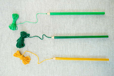 Three threads of yellow, green and light green colors go from srtands to pencils of the same colors on natural linen cloth. Concept of colored threads as artistic tools.の写真素材