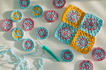 Top view of crochet motifs and a hook with crochet chain started,  on white surface with  bold...