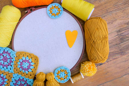 Layout of balls of yarn, embroidery hoop with blank tightened fabric, crochet patterns, spools of thread on wooden surface. Concept of love for hand made and crafts.の写真素材