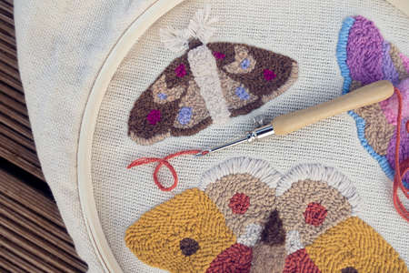 Closeup of embroidered butterflies on two-thread cloth in a hoop with punch needle and brick-red thread inside of it. Punch needle embroidery.の写真素材