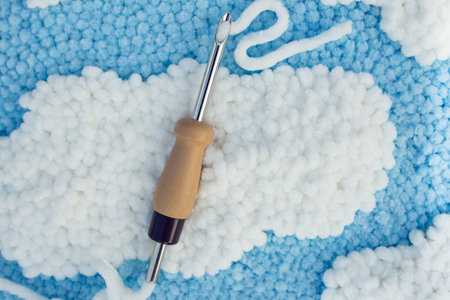 Closeup of punch needle with wooden handle and velour thread run through an eyelet on soft velour embroidered spot. Punch needle embroidery concept.の写真素材