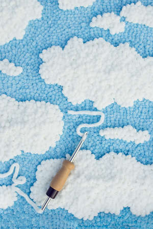 View of embroidered carpet of blue color with white spots and a punch needle with white velour thread run through its eyelet. Punch needle embroidery concept.の写真素材