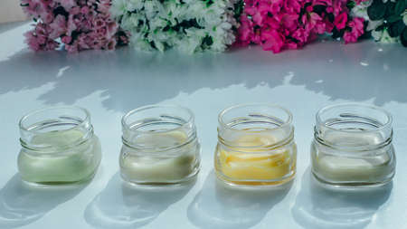 Four jars of cosmetic cream of different colors with a flowers background. Herbal cosmetics concept.の写真素材