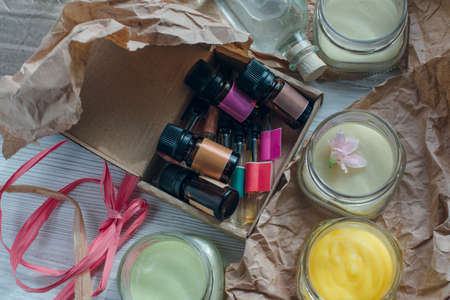 A small box with essential oils testers with cream jars, brown craft paper, ribbons on a white wooden board. Aromatherapy and herbal essenses concept.の写真素材