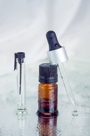 Closeup of a brown-glass flask, glass-dropper, tester, all with black lids, covered with water drops...