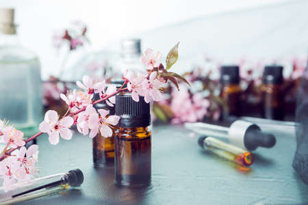 Closeup of brown-glass plain flask with black cover and a tender spray of blosoom on it. Blurred flowers, cosmetic flasks and testers in the background.の写真素材