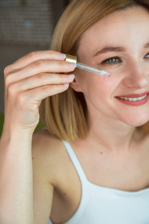 Closeup of caucasian woman's hand with cosmetical glass dropper upon her face. Cosmetology, skin care and treatment.の写真素材
