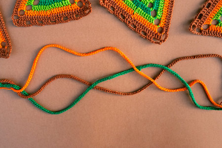 Top view of tree crochet cords and parts of multicolored crochet motifs on beige background. Textile...