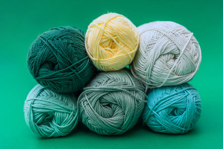 Side view of six balls of yarn in two rows, one on another, placed on green background. Colors are green with yellow and beige accents.の写真素材