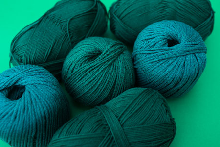 Close view of dark green balls of yarn with different types of thread on green background. Woolen and cotton yarn.の写真素材
