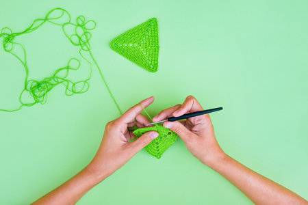 Hands making green triagle crochet  motif on light green background. Simple and minimalistic view on crocheting.の写真素材