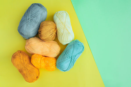Top view of multicolored yarn skeins on yellow surface and an empty space on the right side in light green color. Materials for fiber art and craft.の写真素材