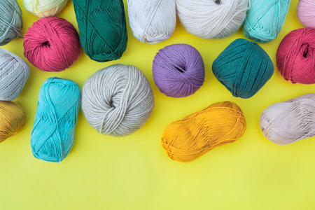 Layout of different balls and skeins of yarns on bright yellow background. Multicolored fibers for...
