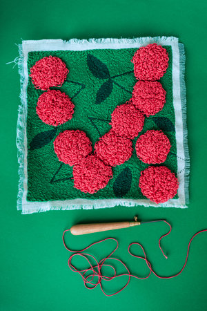 Red flowers in punch needle emberoidery technique on green field made on fabric and threaded punch...