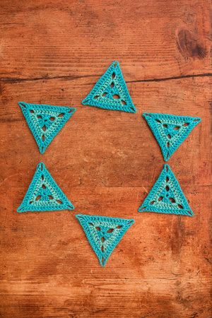 Blue triangle crochet motifs laid in a shape of a circle on grunge wooden surface. Concept of...