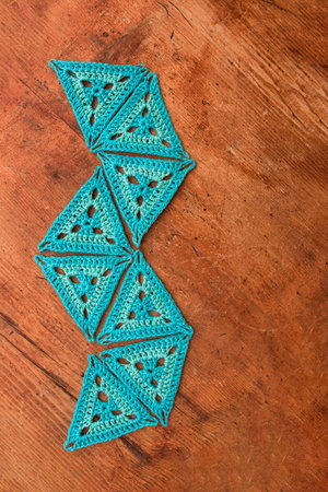 Top view of blue triangle crochet patterns laid in a random geometric shape on wooden surface. Idea...