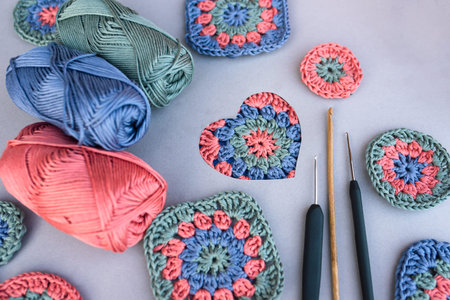 Crochet pattern in a heart and three different hooks with other patterns and skeins of yarn around...