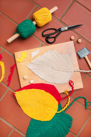 Layout of materials and supplies for macrame, including four big multicolored macrame leaves on the...