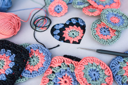Closeup of crochet hook with black handle and different crochet samples, yarns and heart symbol...